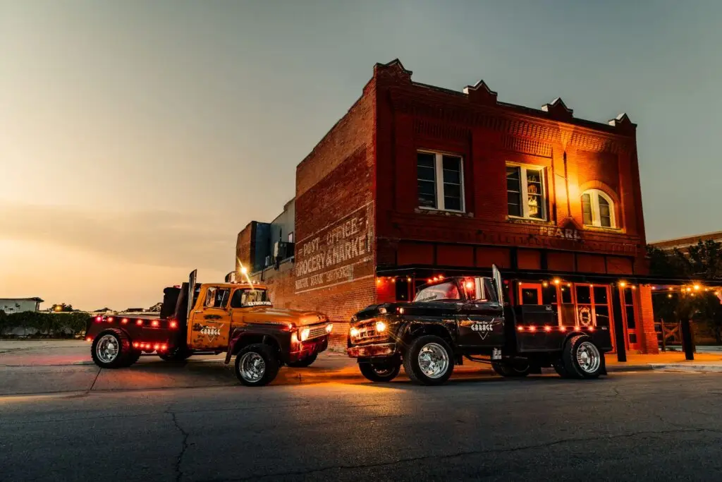 Black and orange custom diesel trucks parked at dusk in front of a lit brick building