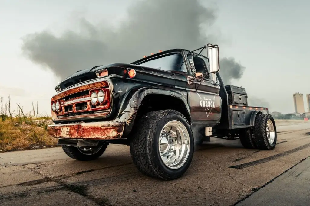Weathered black Chevrolet diesel truck on pavement with exhaust smoke behind it