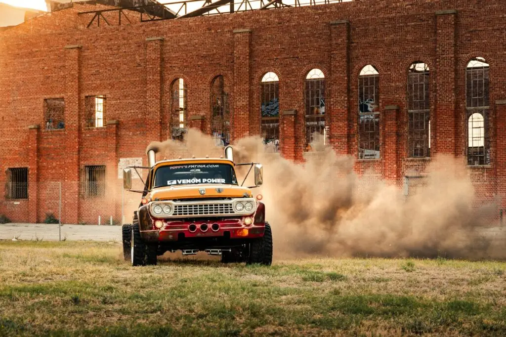 Orange diesel truck kicking up dust in front of a brick warehouse