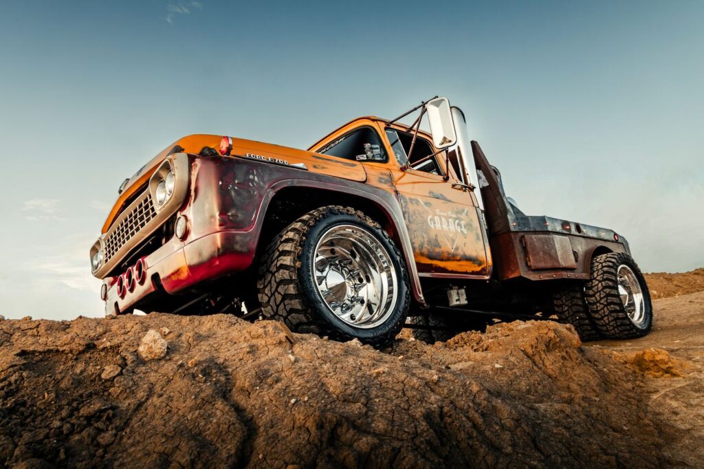 Orange flatbed diesel truck perched on a dirt hill under a dramatic sky