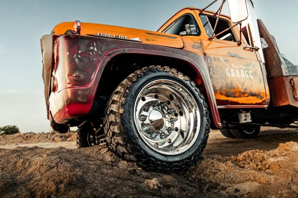Low angle of an orange diesel truck with polished wheels climbing a dirt mound