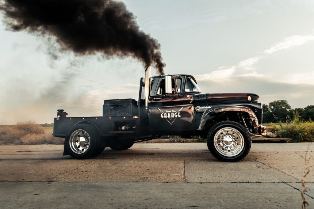 Black flatbed diesel truck rolling coal with thick black exhaust smoke