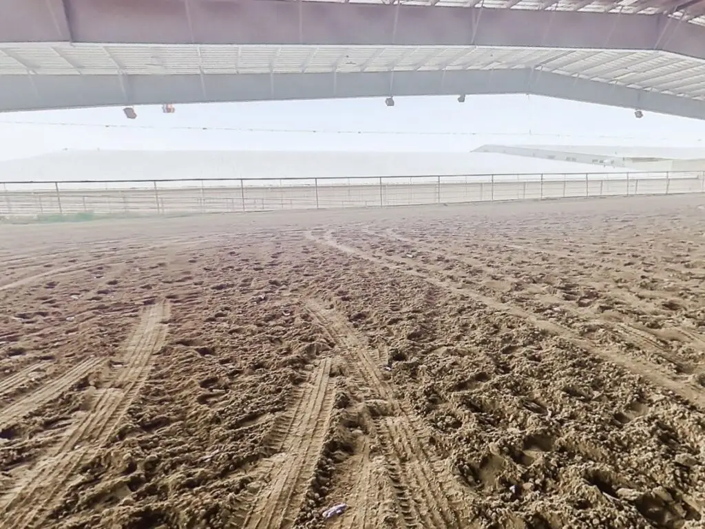 The empty covered outdoor dirt arena with an open-air roof
