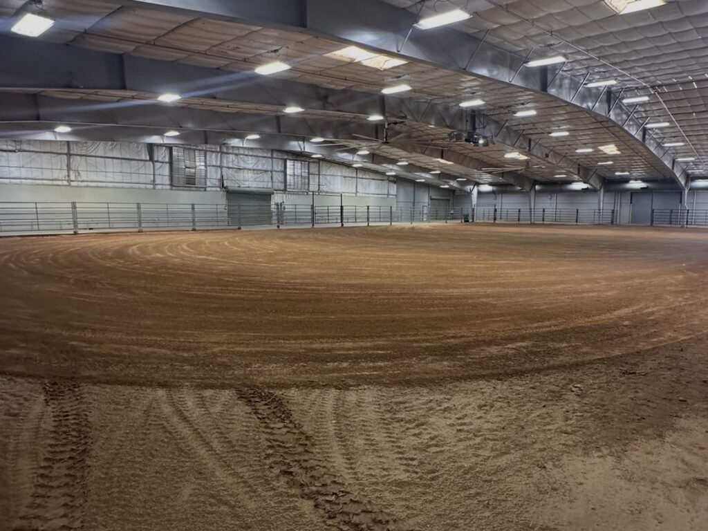 The empty indoor dirt arena under a steel roof structure